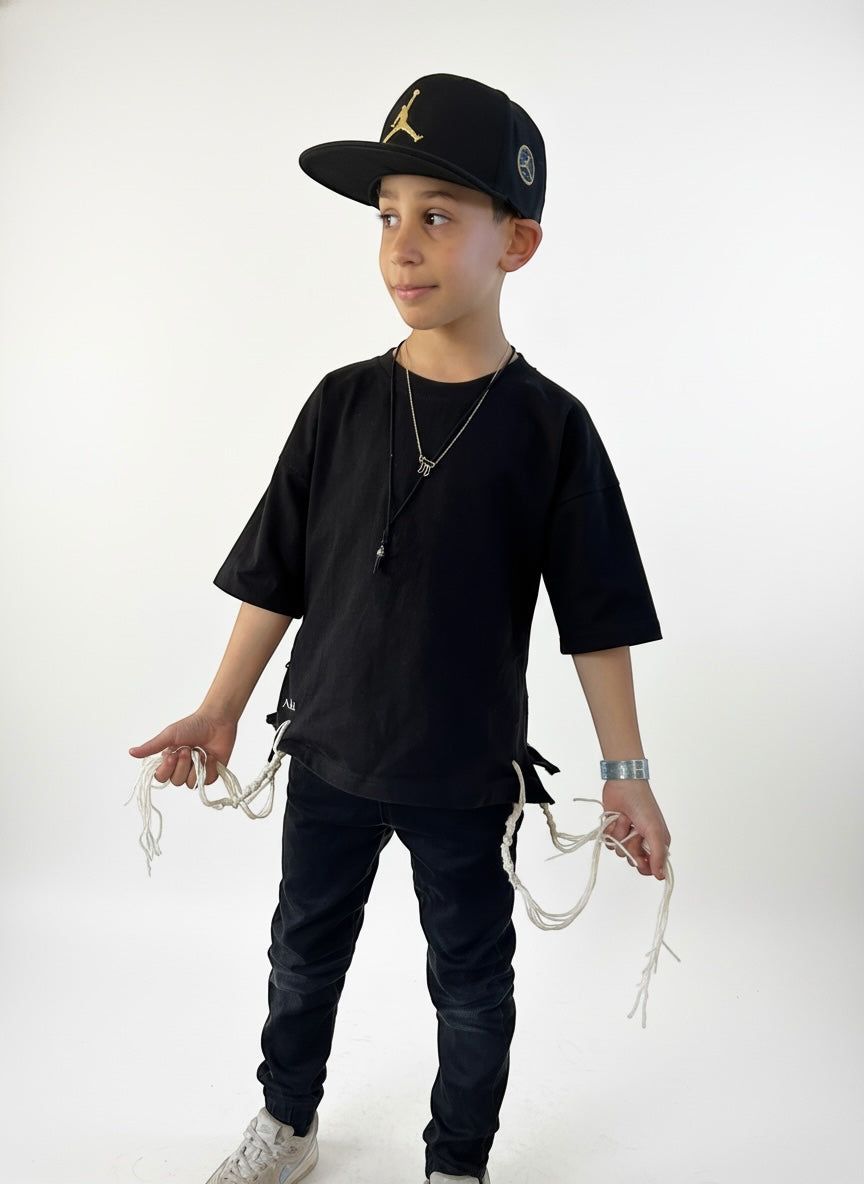T-shirt tsitsit enfant noir oversize NAHAL porté par un garçon, vue de face avec tsitsit blancs